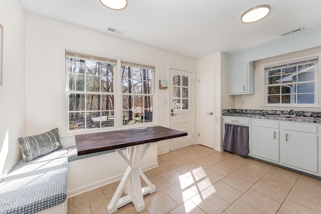 kitchen with light tile patterned flooring, visible vents, white cabinets, and a sink