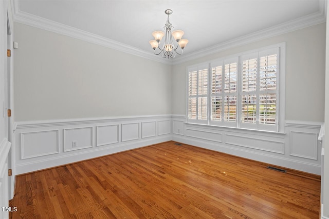 spare room featuring visible vents, a notable chandelier, wood finished floors, and ornamental molding