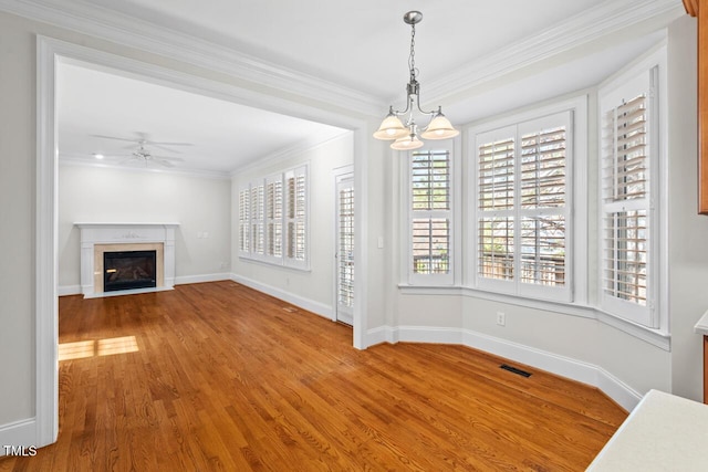 unfurnished dining area featuring visible vents, ornamental molding, ceiling fan with notable chandelier, and wood finished floors