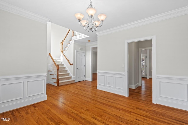 unfurnished dining area with stairway, wood finished floors, crown molding, a decorative wall, and a chandelier