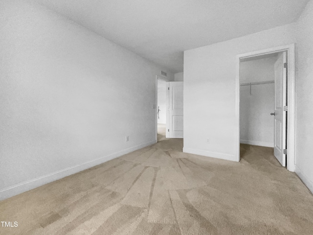 unfurnished bedroom with visible vents, a closet, baseboards, light colored carpet, and a spacious closet