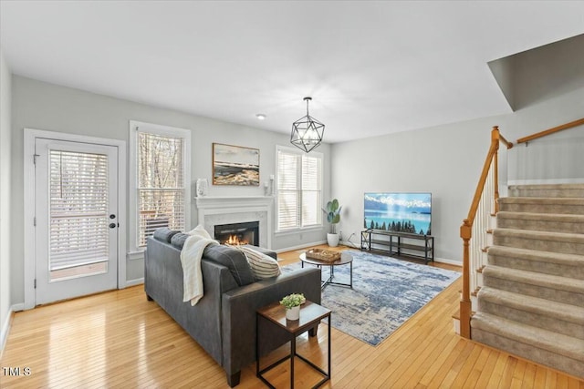 living area featuring light wood finished floors, baseboards, stairway, a glass covered fireplace, and a notable chandelier