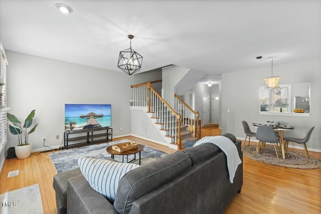 living area featuring stairway, visible vents, baseboards, light wood-style floors, and a notable chandelier