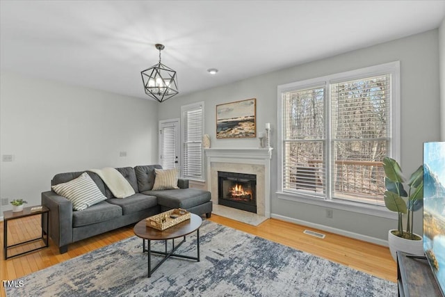 living room featuring visible vents, a notable chandelier, wood finished floors, a high end fireplace, and baseboards