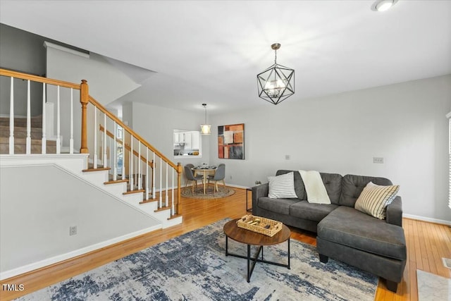 living area featuring a chandelier, baseboards, wood finished floors, and stairs