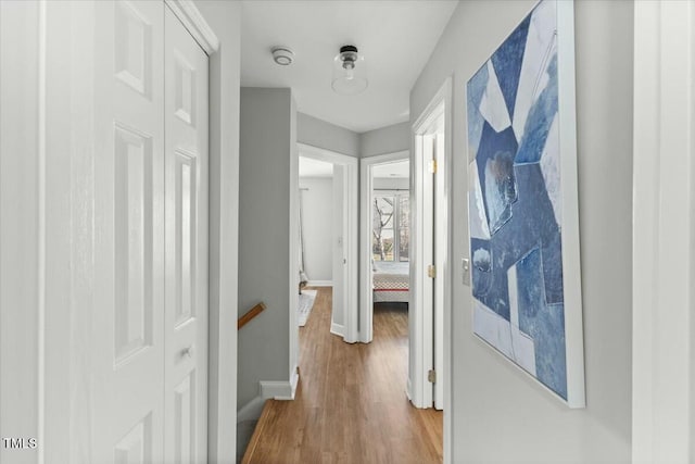 hallway with an upstairs landing, wood finished floors, and baseboards