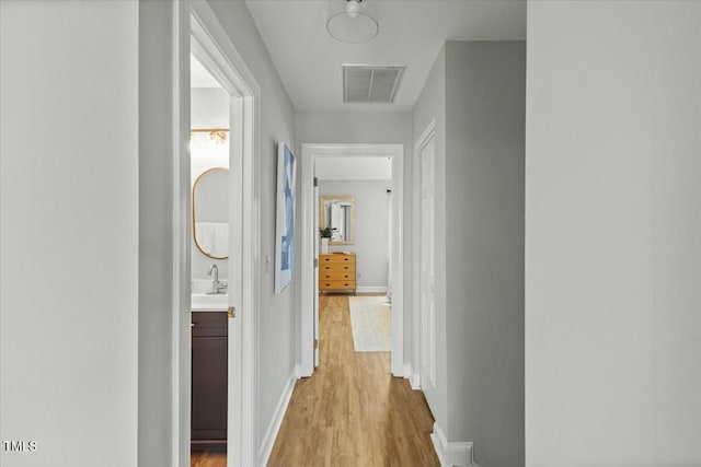 corridor with light wood-style flooring, baseboards, visible vents, and a sink