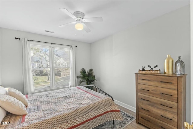 bedroom featuring ceiling fan, visible vents, baseboards, and wood finished floors