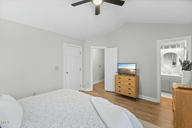 bedroom with baseboards, lofted ceiling, ensuite bathroom, wood finished floors, and a sink