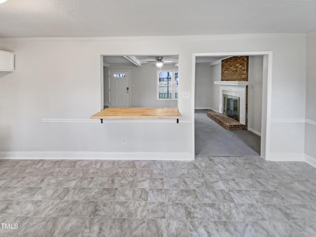 interior space featuring ceiling fan, a fireplace, crown molding, and baseboards