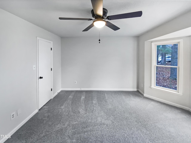 empty room featuring a ceiling fan, baseboards, and dark carpet