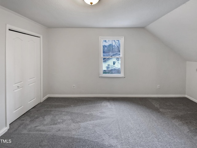 unfurnished bedroom with lofted ceiling, a textured ceiling, a closet, carpet flooring, and baseboards