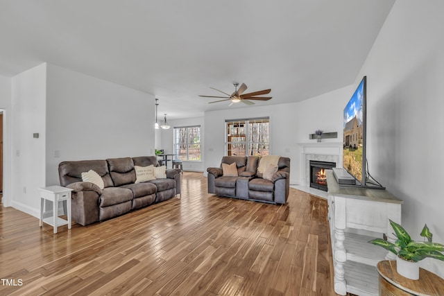 living area featuring baseboards, a fireplace with flush hearth, wood finished floors, and a ceiling fan