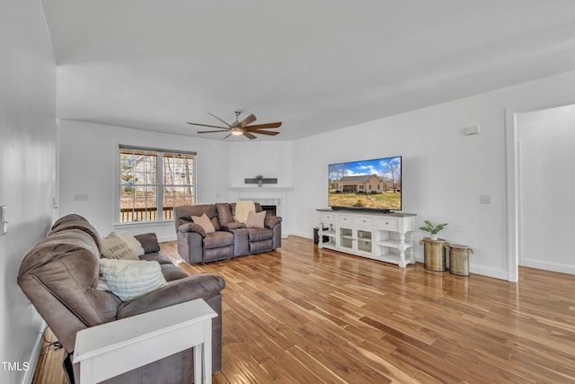 living area featuring wood finished floors, a ceiling fan, baseboards, and a premium fireplace