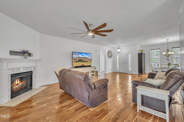 living room featuring a high end fireplace, ceiling fan with notable chandelier, light wood-type flooring, and baseboards