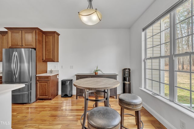 kitchen with brown cabinets, freestanding refrigerator, light wood-style floors, light countertops, and baseboards