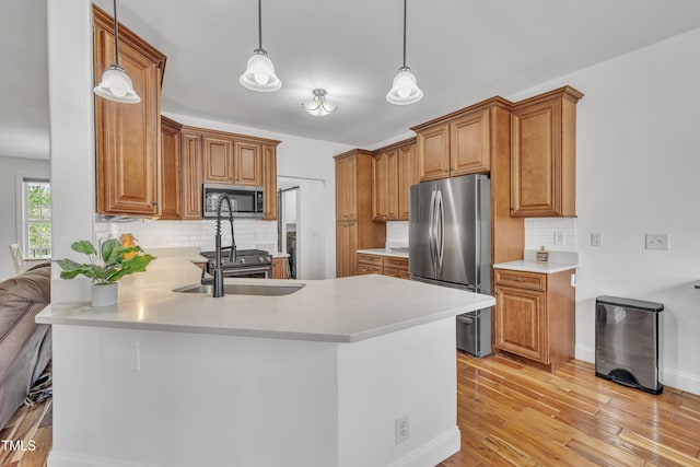 kitchen featuring light countertops, appliances with stainless steel finishes, a peninsula, light wood-style floors, and brown cabinetry