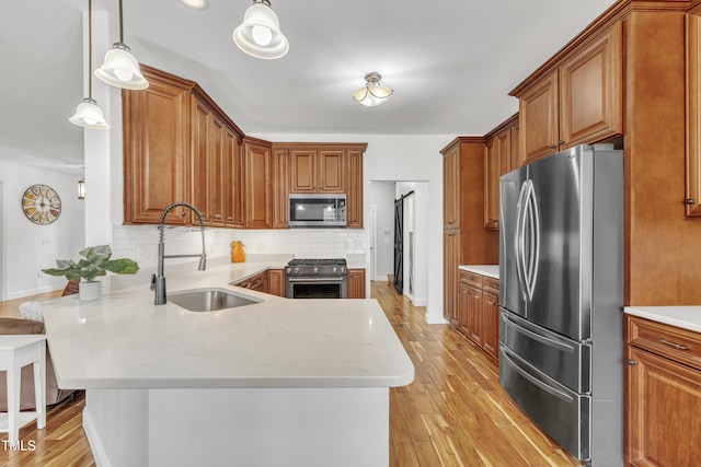 kitchen with backsplash, light wood-style flooring, appliances with stainless steel finishes, a peninsula, and a sink