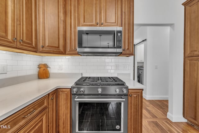 kitchen with light wood-style floors, tasteful backsplash, appliances with stainless steel finishes, and light countertops