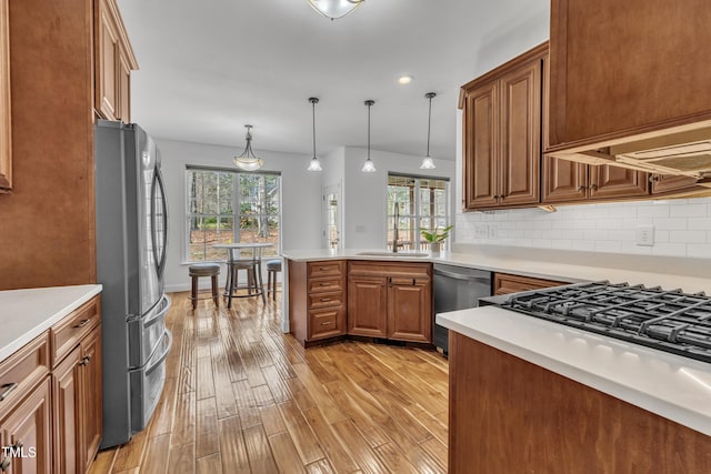 kitchen featuring light wood-type flooring, brown cabinets, a sink, tasteful backsplash, and stainless steel appliances