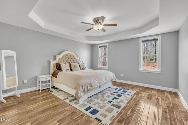 bedroom featuring light wood-style flooring, a raised ceiling, baseboards, and ceiling fan