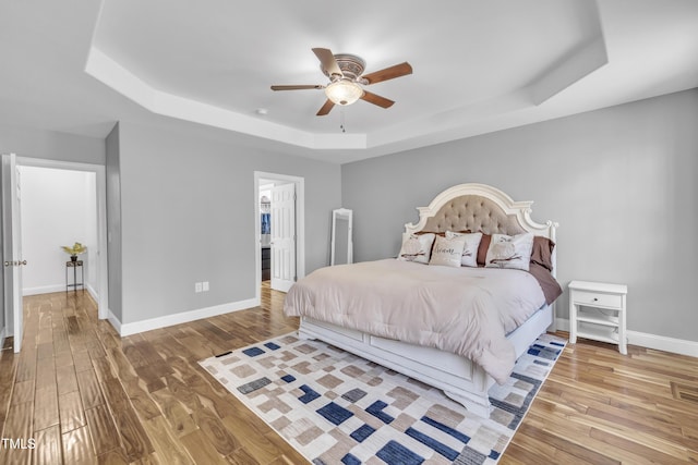 bedroom with a tray ceiling, baseboards, and wood finished floors