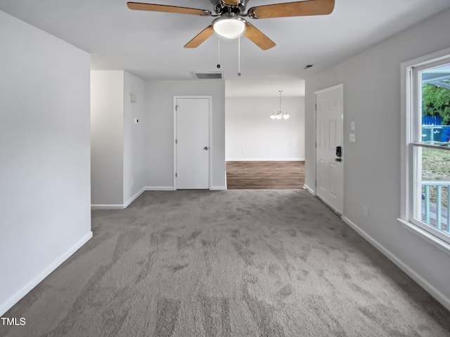 empty room with visible vents, ceiling fan with notable chandelier, carpet flooring, and baseboards