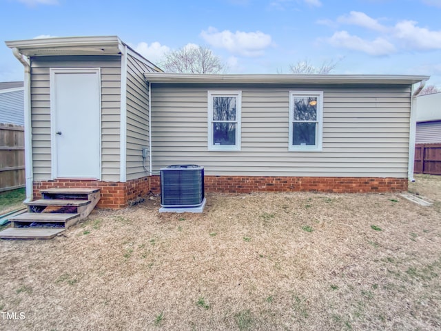 back of property with central air condition unit, entry steps, a lawn, and fence