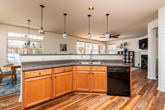 kitchen featuring light wood-type flooring, a sink, dark countertops, a fireplace, and dishwasher