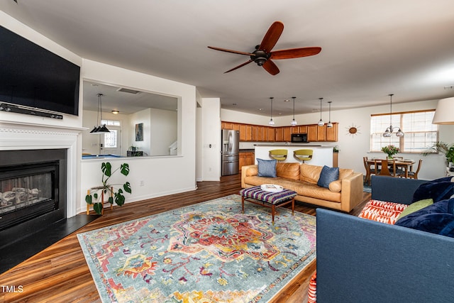 living area featuring a ceiling fan, baseboards, visible vents, dark wood finished floors, and a fireplace