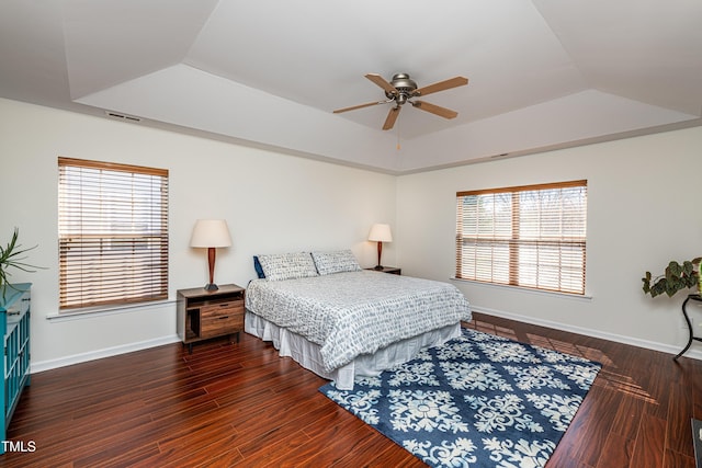 bedroom featuring a tray ceiling, baseboards, visible vents, and wood finished floors