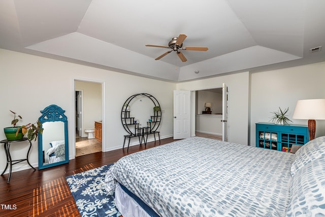 bedroom with visible vents, baseboards, a tray ceiling, and wood finished floors