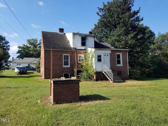 rear view of house with brick siding, a lawn, entry steps, and a chimney