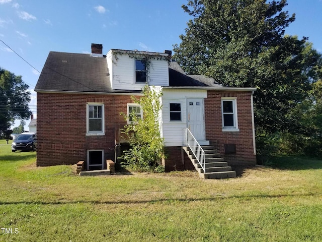 back of property featuring brick siding, entry steps, a chimney, and a yard