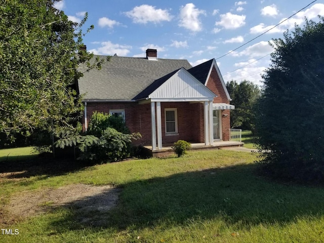 view of property exterior featuring a porch, a yard, a shingled roof, brick siding, and a chimney