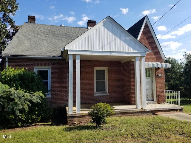 view of front facade featuring brick siding, a porch, a chimney, and a shingled roof