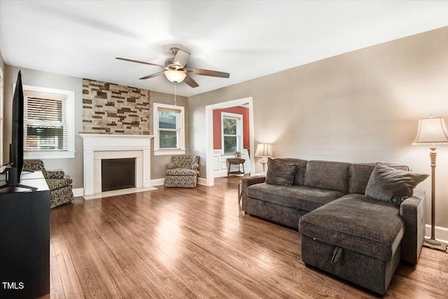 living area with baseboards, a large fireplace, ceiling fan, and wood finished floors