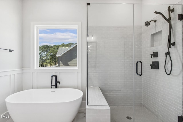 bathroom with a soaking tub, a shower stall, a decorative wall, and a wainscoted wall