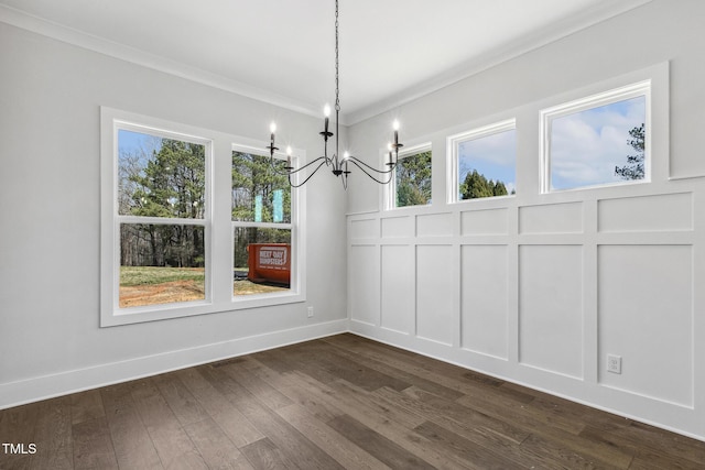 unfurnished dining area with baseboards, dark wood-style flooring, crown molding, a decorative wall, and a notable chandelier