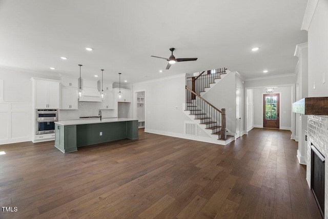9004 Penny Rd, Raleigh, NC 27606 - kitchen with double oven, crown molding, white cabinets, light countertops, and a center island with sink