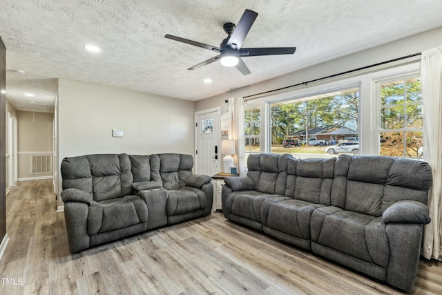 living room with light wood finished floors, visible vents, attic access, a textured ceiling, and a ceiling fan