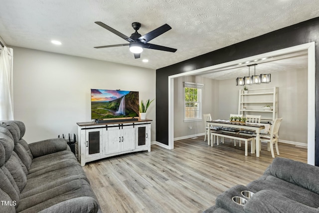 living area with light wood-type flooring, a ceiling fan, a textured ceiling, recessed lighting, and baseboards