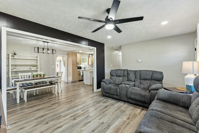 living area featuring a ceiling fan, baseboards, light wood finished floors, recessed lighting, and a textured ceiling