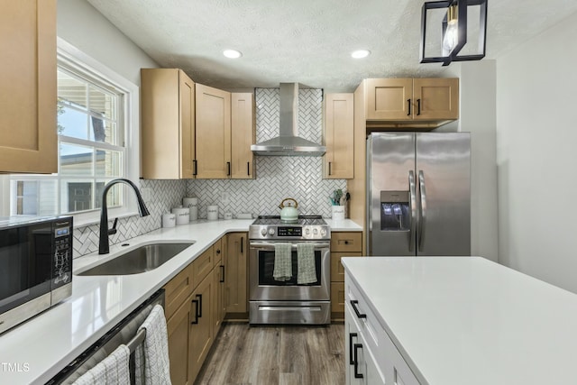 kitchen with wall chimney range hood, light countertops, decorative backsplash, stainless steel appliances, and a sink