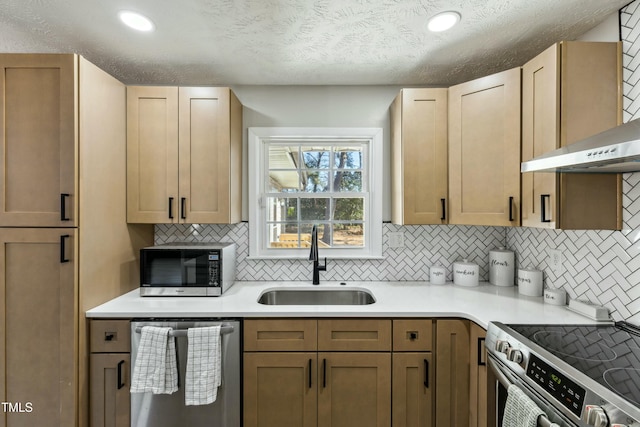 kitchen with a sink, light countertops, appliances with stainless steel finishes, wall chimney exhaust hood, and tasteful backsplash