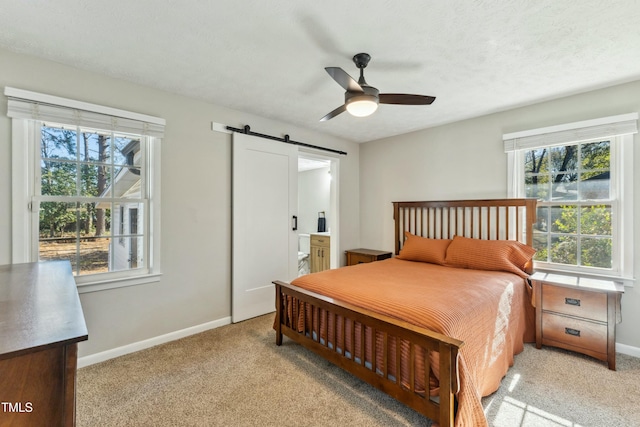 bedroom featuring light carpet, ensuite bathroom, a barn door, baseboards, and ceiling fan