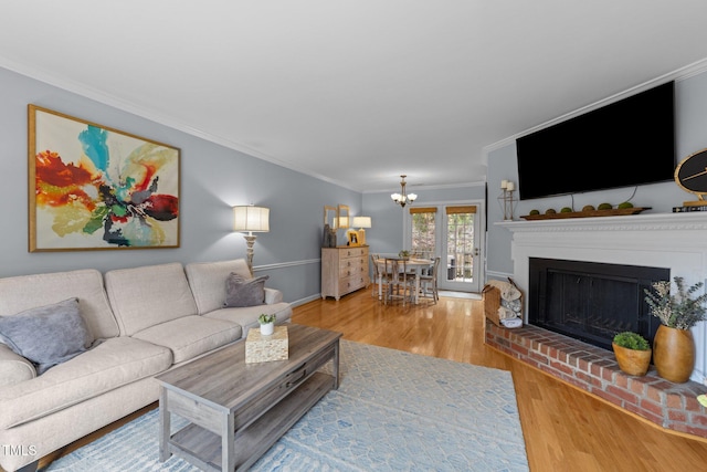 living room with a notable chandelier, a fireplace with raised hearth, crown molding, and wood finished floors