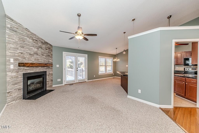 living room featuring baseboards, light colored carpet, lofted ceiling, a stone fireplace, and ceiling fan with notable chandelier