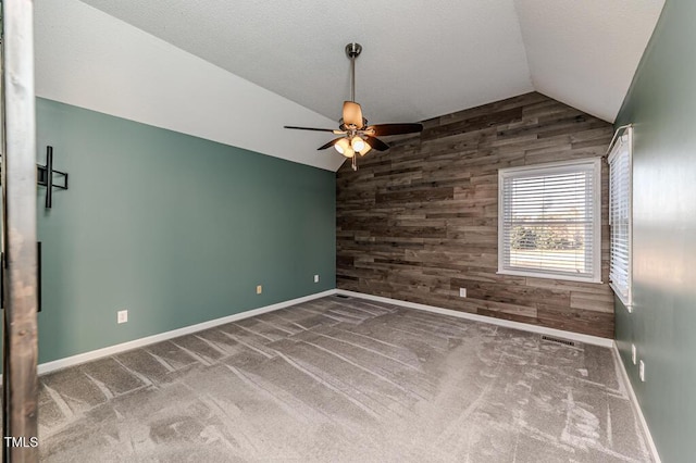 empty room featuring wooden walls, carpet flooring, lofted ceiling, ceiling fan, and an accent wall