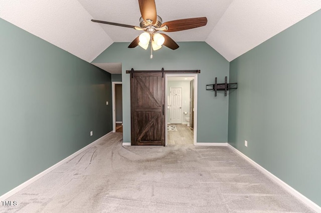 unfurnished bedroom with baseboards, lofted ceiling, a barn door, and carpet